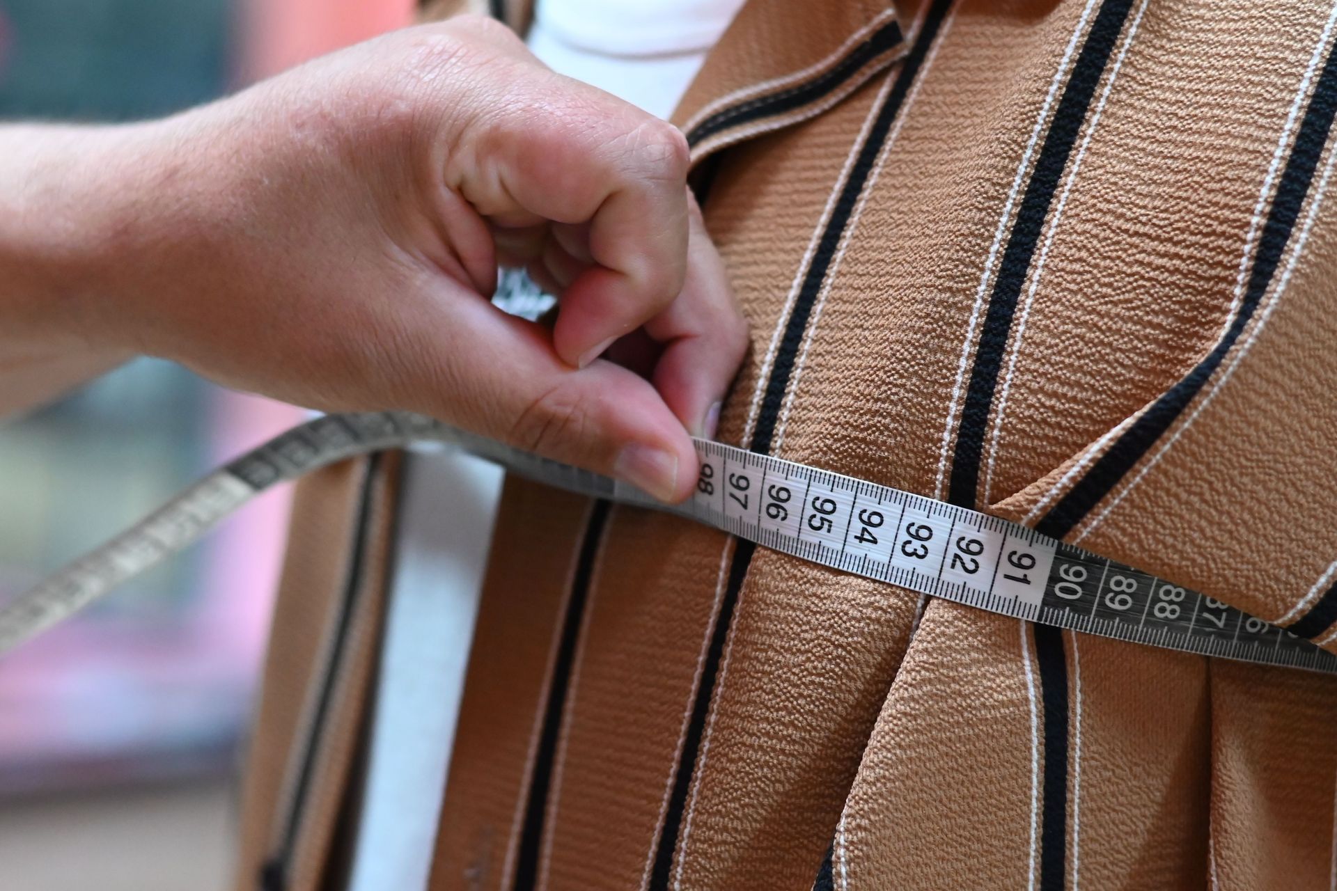 A close-up of a tailor measuring fabric with a tape, showcasing precision and craftsmanship.
